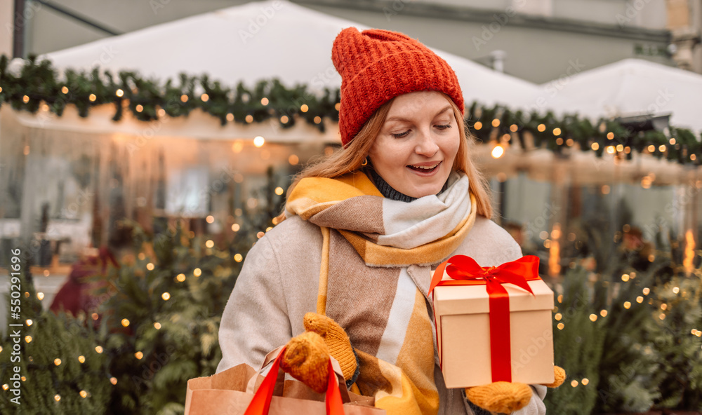 Happy young attractive woman with paper bags and gift boxes in hands after Christmas shopping in mall. Cheerful beautiful girl hold shopping bags and present boxes in hands. Winter holidays sale Happy young attractive woman with paper bags and gift boxes in hands after Christmas shopping in mall. Cheerful beautiful girl hold shopping bags and present boxes in hands. Winter holidays sale