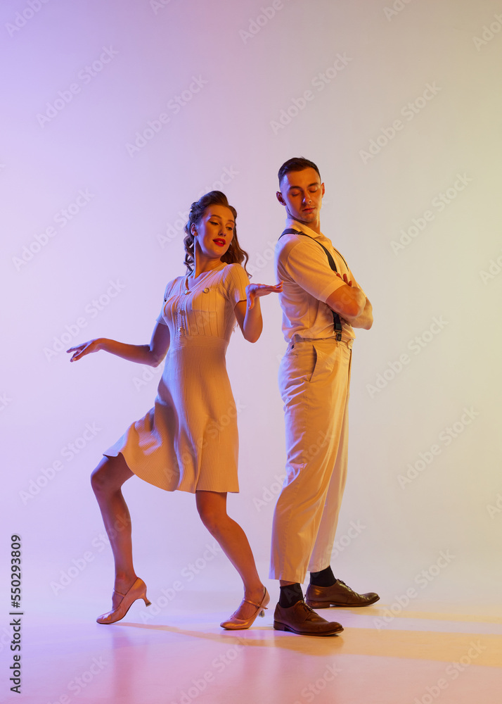 Beautiful girl and man in retro style costumes dancing incendiary dances isolated on gradient lilac color background in neon light. Concept of art, 60s, 70s culture