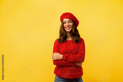 Young charming woman with waving hair wearing red beret and red shirt posing over yellow background 