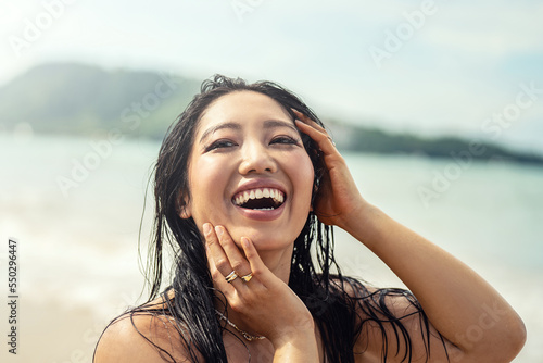 Portrait of beautiful young asian woman with amazing toothy smile. Girl with wet hair enjoying sunny day on the beach. Happy holiday lifestyle concept. Real people emotions.
