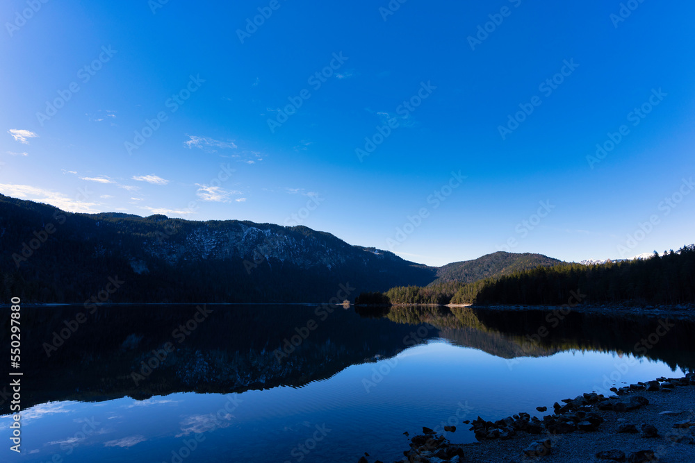Beautiful lake in the mountains mirroring reflecting and a blue bright sky with some clouds - Eibsee, Alps