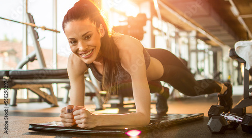 Attractive fitness girl doing plank exercise on mat at gym. Smiling sporty young woman doing plank exercise.