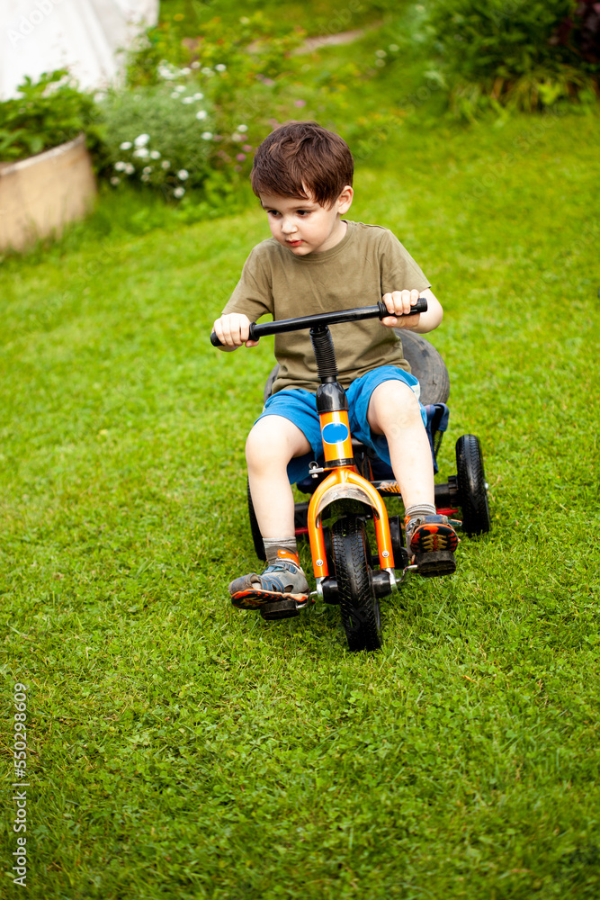 a three-year-old boy learns to ride a tricycle on the grass from his grandparents in the country a three-year-old boy learns to ride a tricycle on the grass from his grandparents in the country