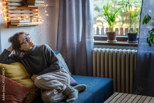 Obraz na płótnie Young adult happy cheerful woman 30s in warm sweater and eyeglasses sitting on sofa enjoying resting and relaxing with her eyes closed w salonie