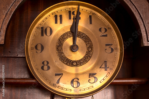 Close-up of the golden face of an old clock showing twelve o'clock (noon, midnight).