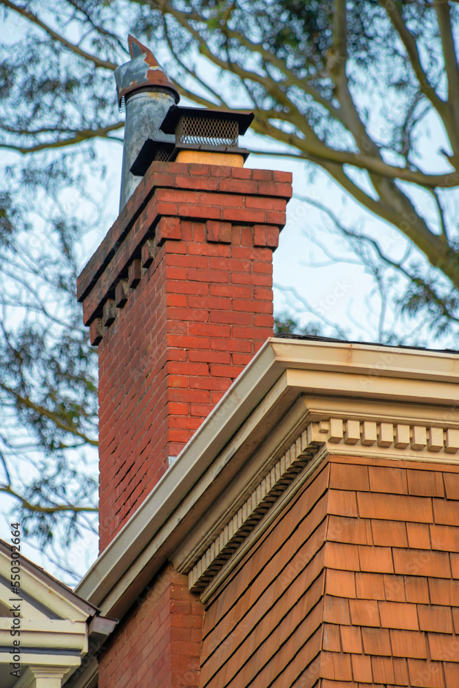 Brick chimneys with decorative yellow facade in late afternoon sunlight with visible trees in background with metal chimey vents Brick chimneys with decorative yellow facade in late afternoon sunlight with visible trees in background with metal chimey vents
