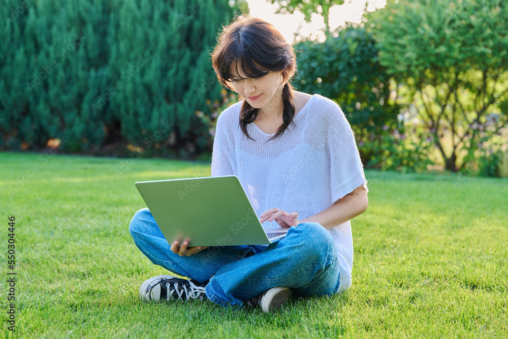 Teenage girl sitting on the grass using a laptop Teenage girl sitting on the grass using a laptop