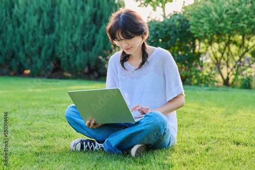 Teenage girl sitting on the grass using a laptop