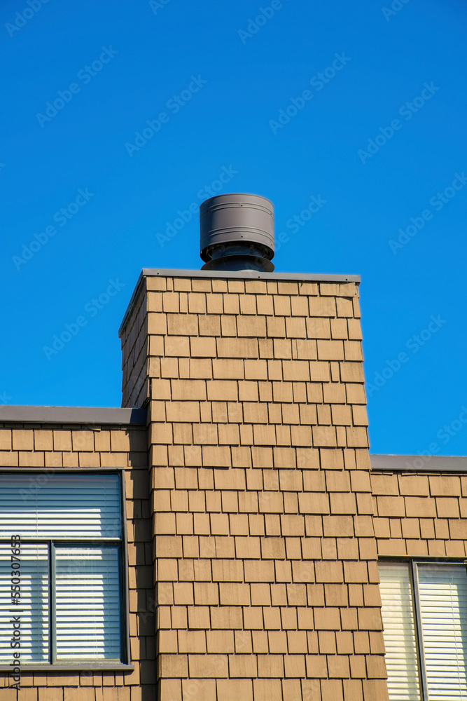 Slatted wooden exterior with visible metal windows with gray metal chimney vent on the top of a house or home in suburbia