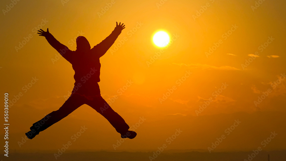 両手両足を広げてジャンプする女性シルエット_夕日背景ワイド 両手両足を広げてジャンプする女性シルエット_夕日背景ワイド