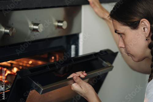 Young woman baking something in oven at home. Woman opening the oven. Domestic kitchen concept.