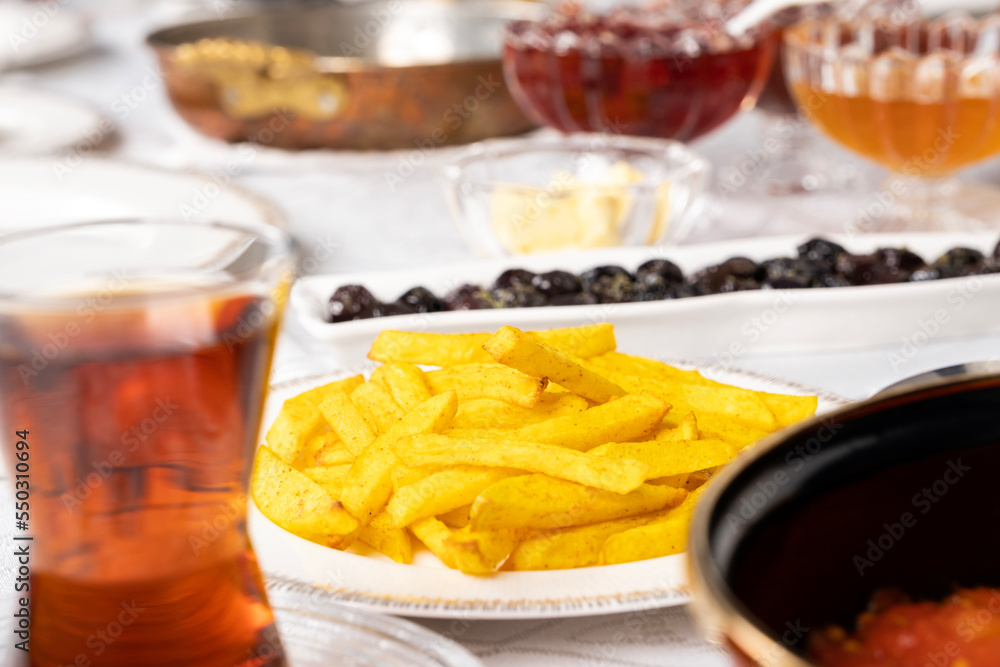 Homemade French fries, selective focus of morning meal table homemade French fries. Gold yellow fried potatoes. Turkish tea and traditional breakfast. Black olive, jam, honey.