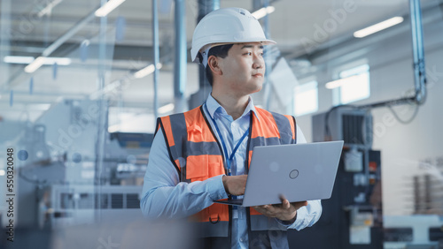 Portrait of an Asian Male Engineer in Orange Safety Vest Working on Laptop Computer at Electronic Manufacturing Factory. Technician Working on Daily Tasks and Research and Development Data.