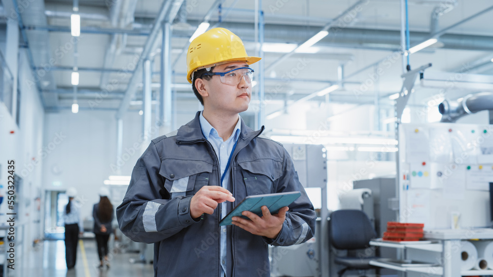 Portrait of a Young Asian Man, Working as an Engineer at a Industrial Facility, Wearing Work Jacket and a Yellow Hard Hat. Heavy Industry Specialist Walking and Using Tablet Computer. Portrait of a Young Asian Man, Working as an Engineer at a Industrial Facility, Wearing Work Jacket and a Yellow Hard Hat. Heavy Industry Specialist Walking and Using Tablet Computer.