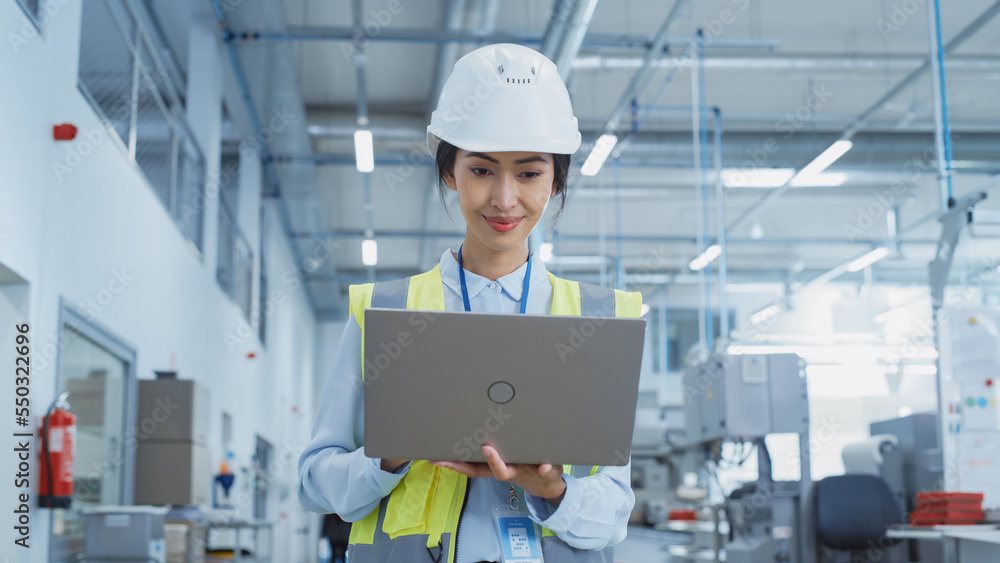 A Happy and Smiling Asian Female Engineer in White Hard Hat Standing with Laptop Computer at Electronic Manufacturing Factory. Successful Employee Focusing on PC Screen A Happy and Smiling Asian Female Engineer in White Hard Hat Standing with Laptop Computer at Electronic Manufacturing Factory. Successful Employee Focusing on PC Screen