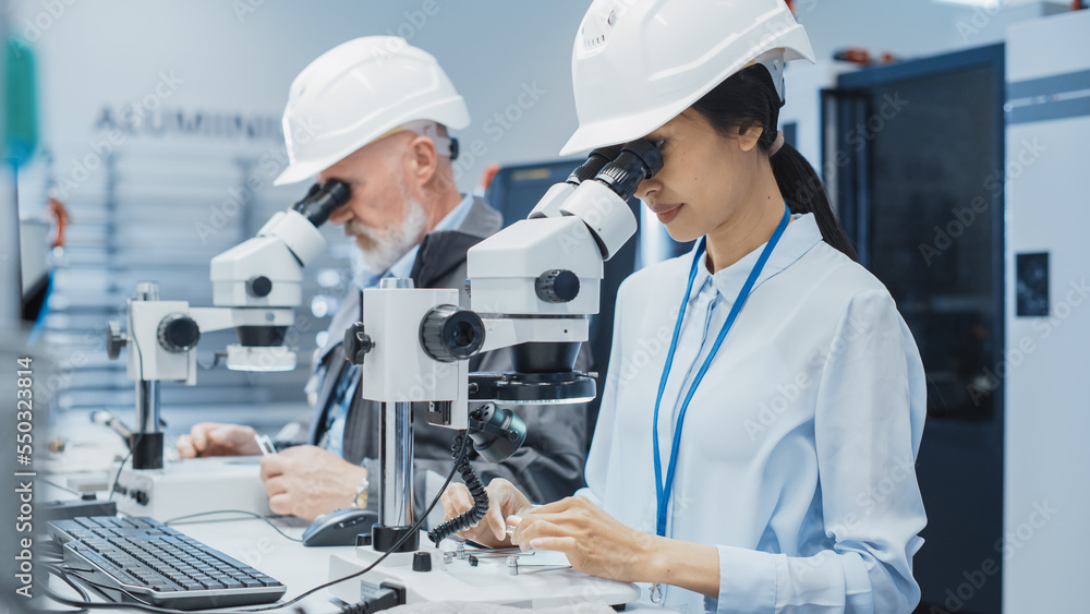 Modern Technology Concept: Two Scientists Examining Small Scale Industrial Equipment Parts Through a Microscope. Technicians Testing New Factory Components for Quality. Modern Technology Concept: Two Scientists Examining Small Scale Industrial Equipment Parts Through a Microscope. Technicians Testing New Factory Components for Quality.