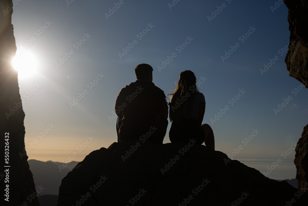 silhouette of a young couple sitting on a rock looking at the sunset