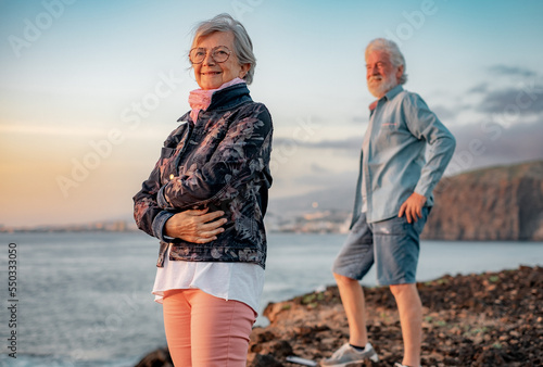 фотографія Carefree senior couple standing at sunset light on the rocks at sea looking at the horizon over water
