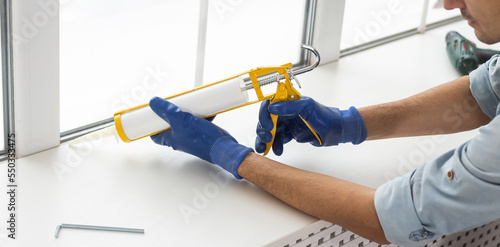 Construction worker sealing window with caulk indoors photo