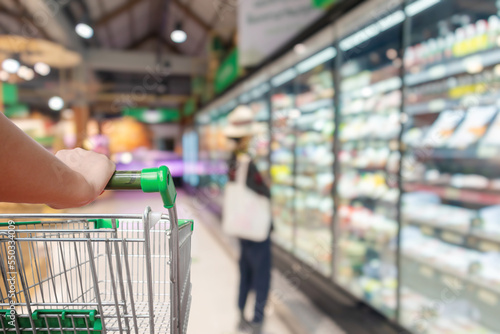 Woman pushing shopping cart with blur supermarket aisle background