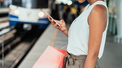 Close Up Photo Of Woman Hands Holding Shopping Bags And Using Mobile Phone At Train Station