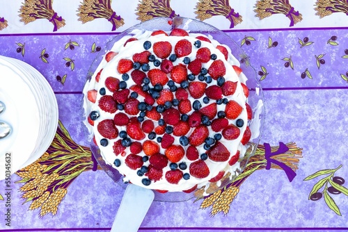 Top view of berries vanilla cream cake with serving white plates on an outdoor colorful table