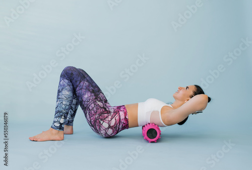 Woman performs myofascial relaxation of the hyperflexible muscles of the back with a massage roller on a blue background. The concept of prevention of back fatigue and self-massage photo