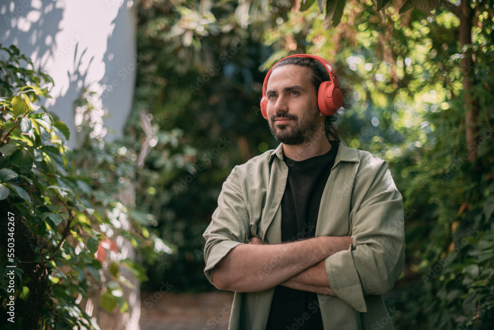 Portrait of a young man in bright large headphones in green foliage.