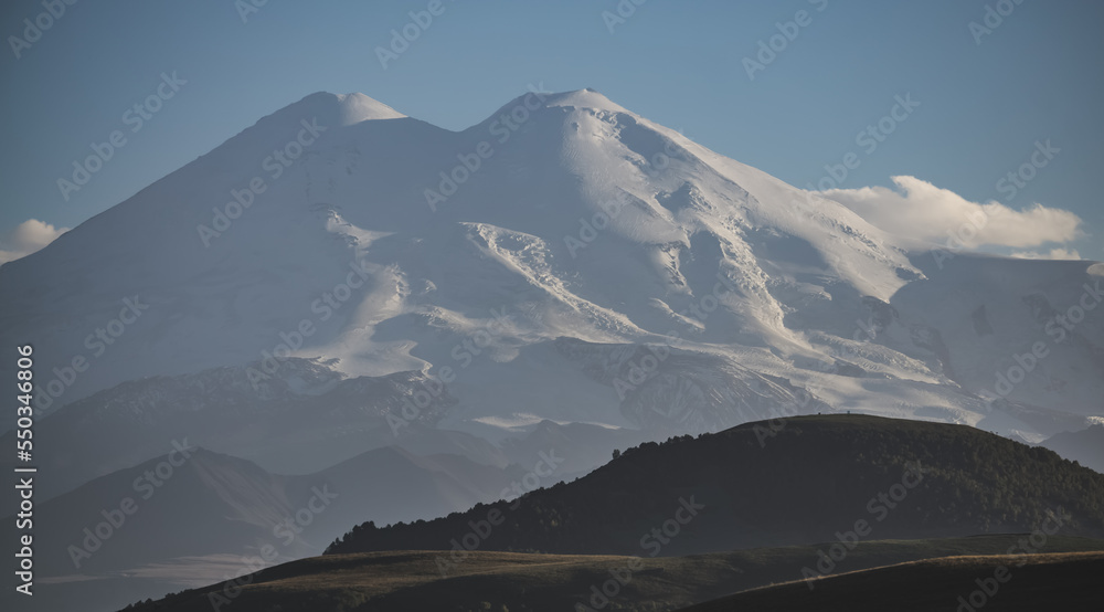 Mount Elbrus illuminated by the setting autumn sun against a clear blue sky, Mount Caucasus with snow and glaciers