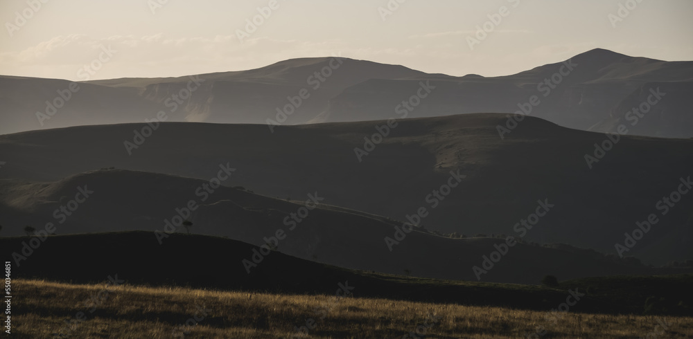Fototapeta premium Panorama of mountain ranges with hills and vegetation on them, at evening sunset lighting