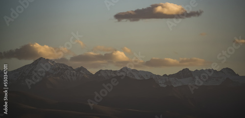 Panorama of a mountain range with peaks with snow and ice at sunset with a cloudy sky, mountain rocky peaks in autumn