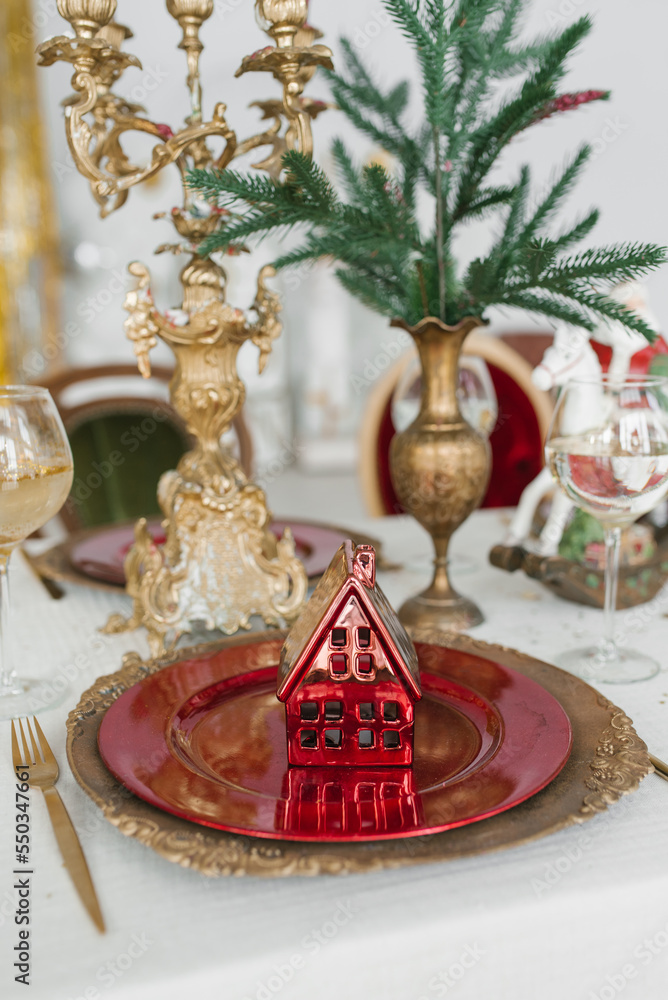 Stylish and beautiful decoration of the serving of a festive Christmas dinner: a toy souvenir red house on a red and gold plate