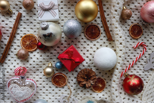 Various colorful Christmas ornaments, small presents and seasonal spices on white knitted blanket. Top view.