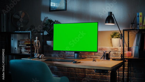 A Modern Personal Computer Monitor with Chroma key Green Screen Display Standing on the Desk of a Cozy Home Office. Living Room Created by Interior Designer with Good Taste and Style.