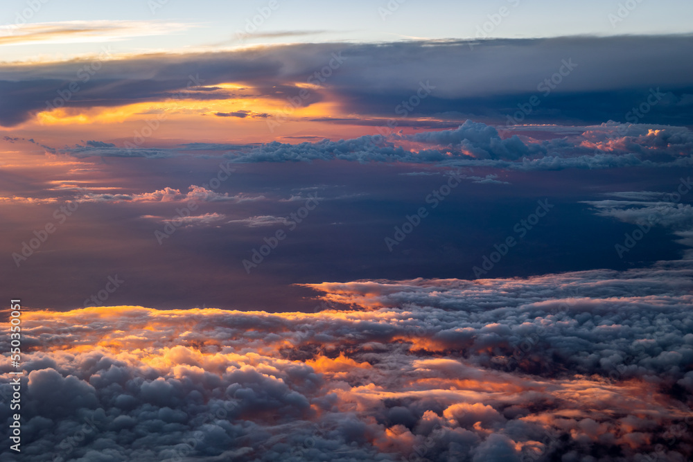 Photo taken from an airplane of the beautiful orange and red colored clouds with a setting sun at the top of the atmosphere