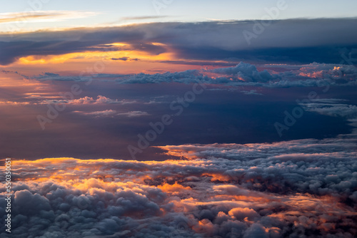 Photo taken from an airplane of the beautiful orange and red colored clouds with a setting sun at the top of the atmosphere