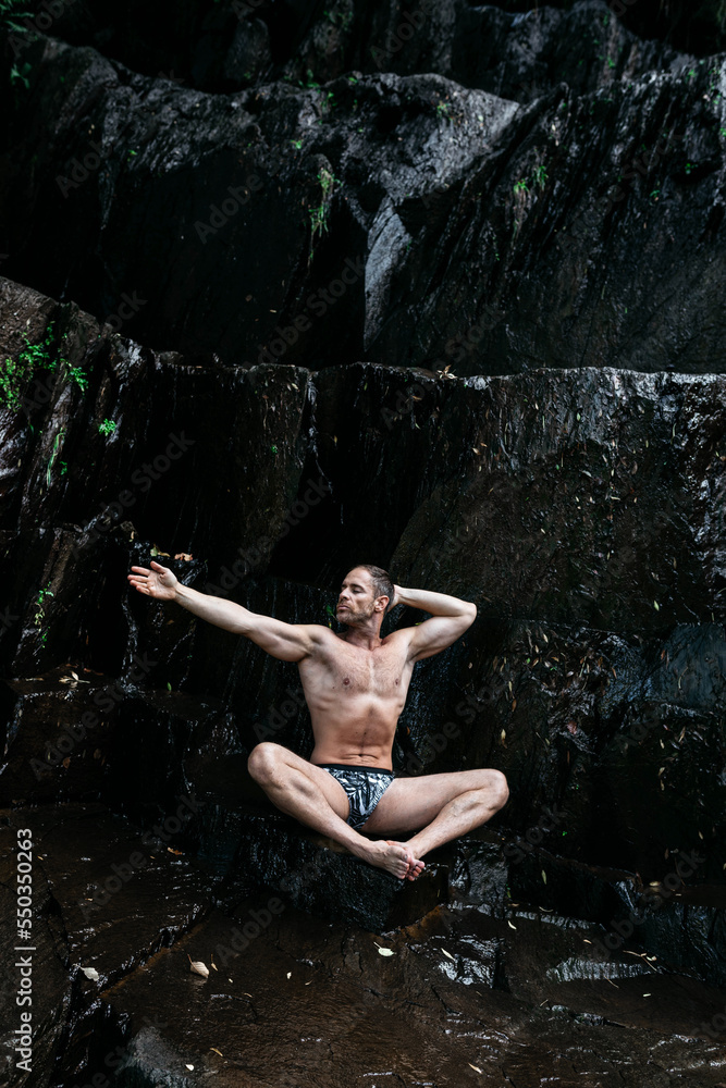 Shirtless male athlete practicing yoga in lotus pose on rocky cliff Shirtless male athlete practicing yoga in lotus pose on rocky cliff