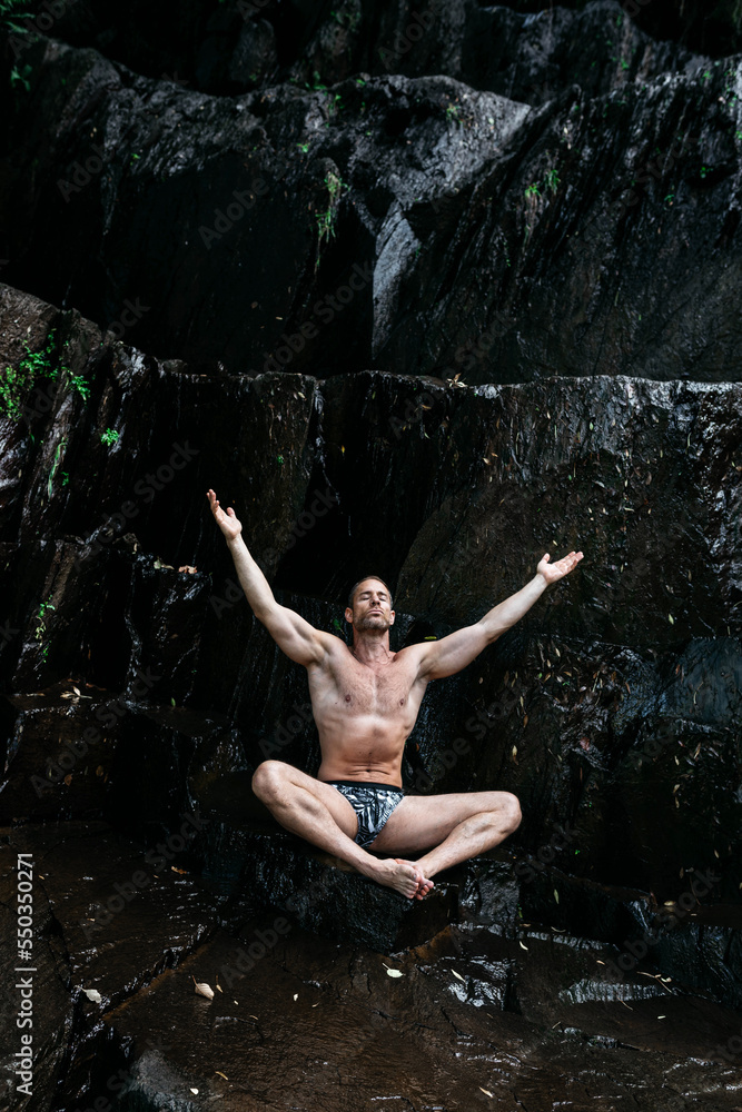 Male athlete doing yoga on stony cliff in Padmasana pose Male athlete doing yoga on stony cliff in Padmasana pose