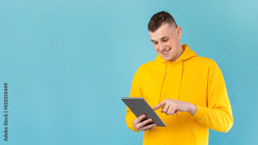 Modern technologies concept. Young man browsing web on digital tablet over blue studio background, panorama, free space Modern technologies concept. Young man browsing web on digital tablet over blue studio background, panorama, free space