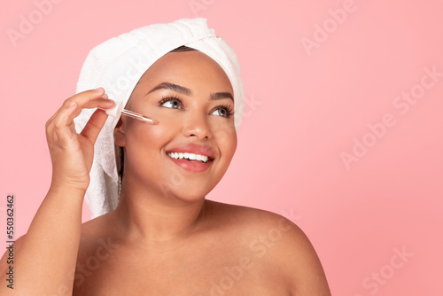 Close up shot of black obese woman using serum in her face care routine, recommending nice beauty product, copy space