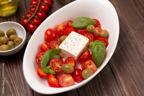Cherry tomatoes with salted cheese, basil and olives in a deep dish prepared for baking