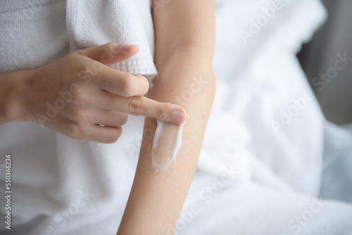 Asia woman sitting on bed and applying cream on her body.