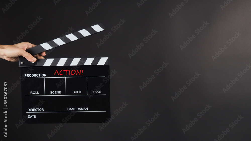 Hand is holding Black clap board on black background.It have word action.