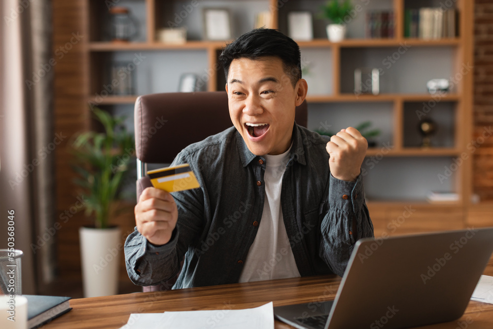 Satisfied surprised excited adult japanese businessman with open mouth hold credit card, make win gesture Satisfied surprised excited adult japanese businessman with open mouth hold credit card, make win gesture