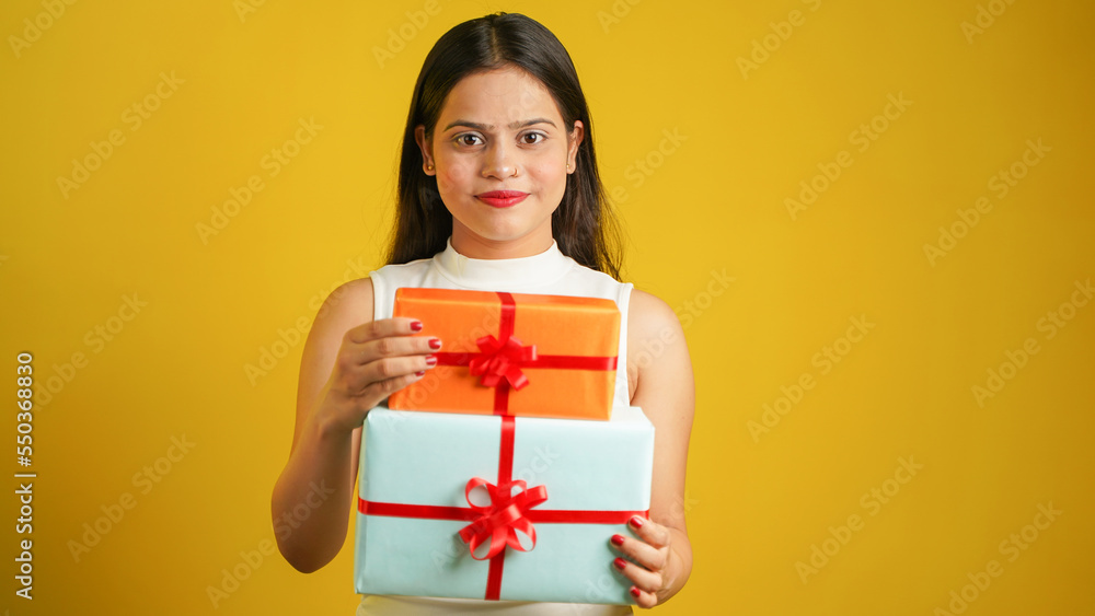 Portrait of an attractive cheerful happy girl holding gift box in hand, Young Asian Indian woman with gifts isolated over color background Portrait of an attractive cheerful happy girl holding gift box in hand, Young Asian Indian woman with gifts isolated over color background
