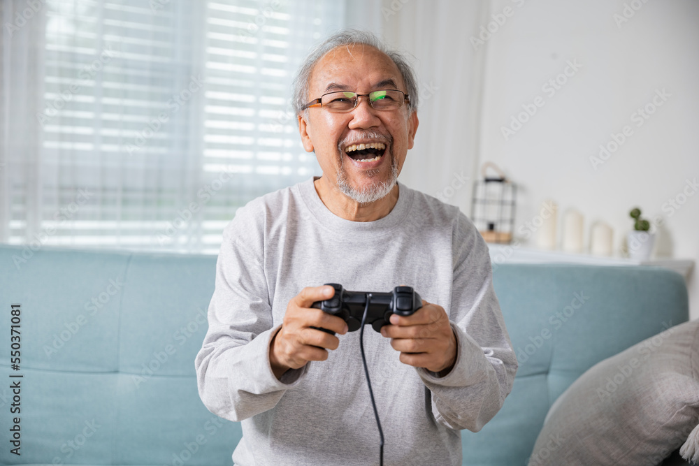 Asian senior old man enjoying holding joystick playing video game at home in living room, mature man hands using game controller, Funny on retirement elderly smile sitting on sofa life gaming Asian senior old man enjoying holding joystick playing video game at home in living room, mature man hands using game controller, Funny on retirement elderly smile sitting on sofa life gaming