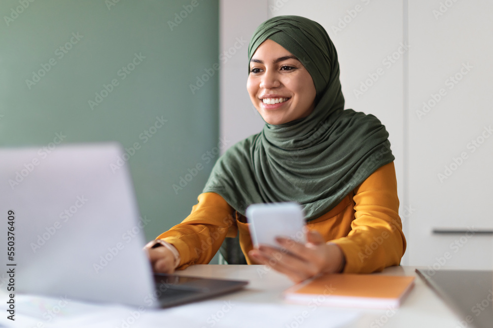 Arab Woman In Hijab Using Smartphone And Laptop While Working At Office Arab Woman In Hijab Using Smartphone And Laptop While Working At Office