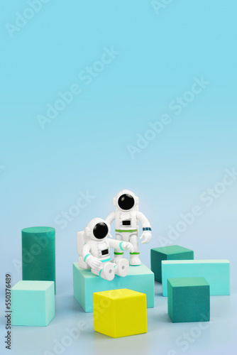 Plastic figurines of astronauts in spacesuit and geometric shapes on blue background. Children's toys astronauts. Fascination with space, study of planets. Space to insert logo or promotional message © Galina