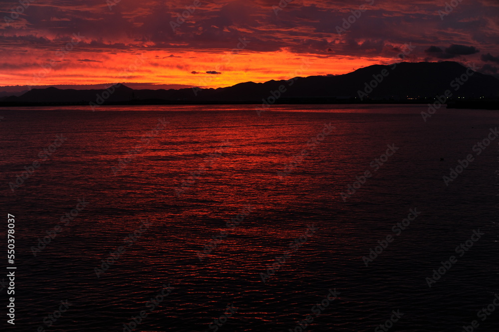 Red, pink, orange and violet sunrise at the seaside during dawn with clouds in the sky and mountains on the shore