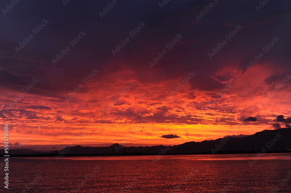Red, pink, orange and violet sunrise at the seaside during dawn with clouds in the sky and mountains on the shore